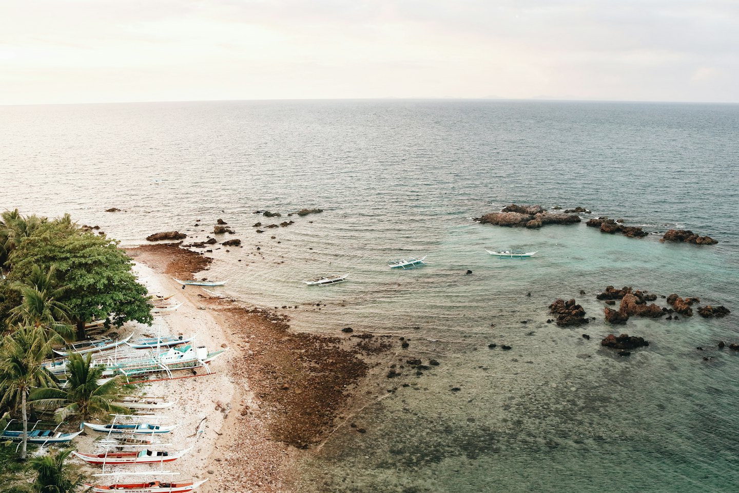 Traditional outrigger boats rest on a sandy tropical beach.