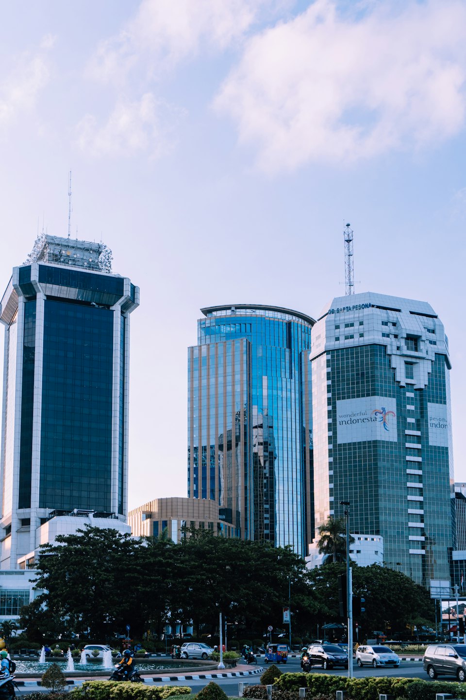Modern skyscrapers overlook a busy urban street and fountain.