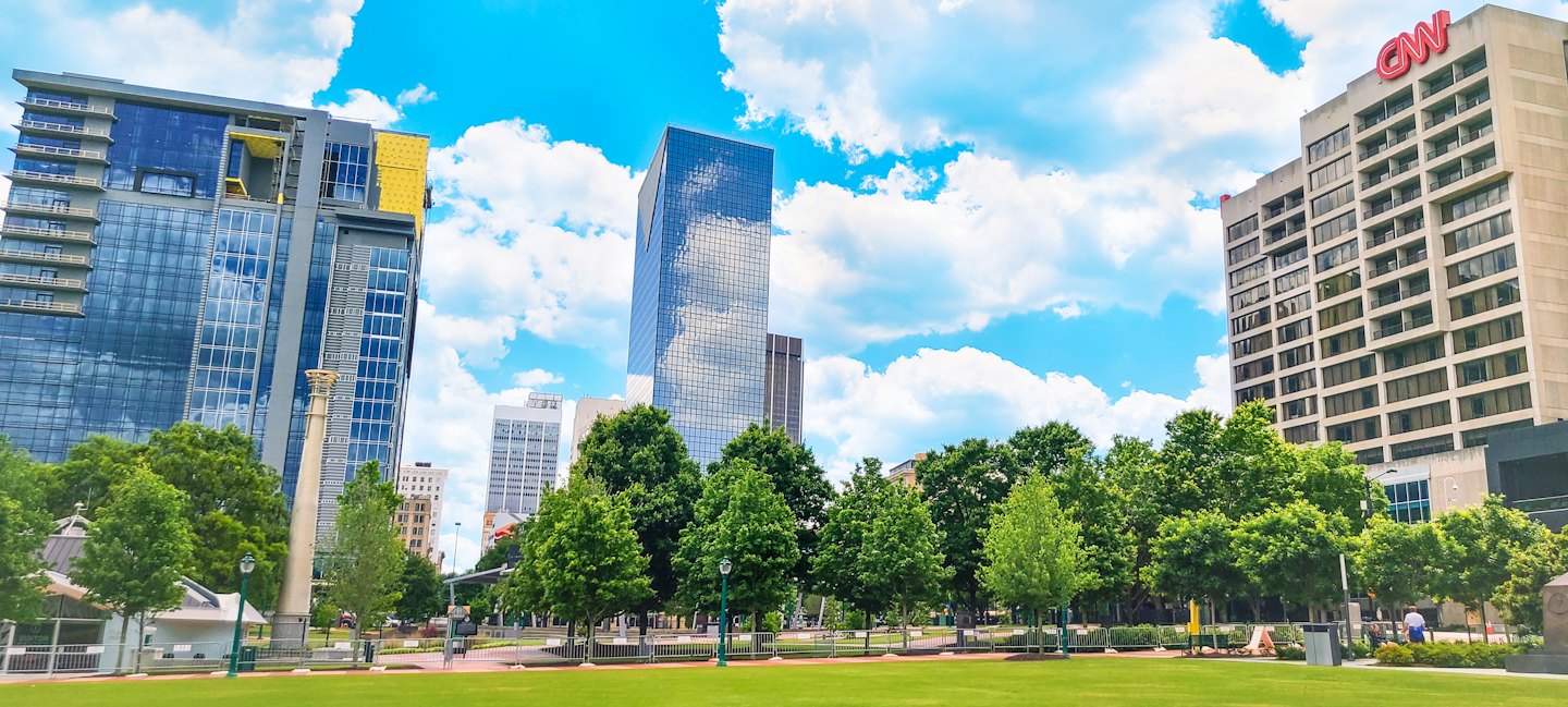 Modern skyscrapers rise above lush trees in a city park.