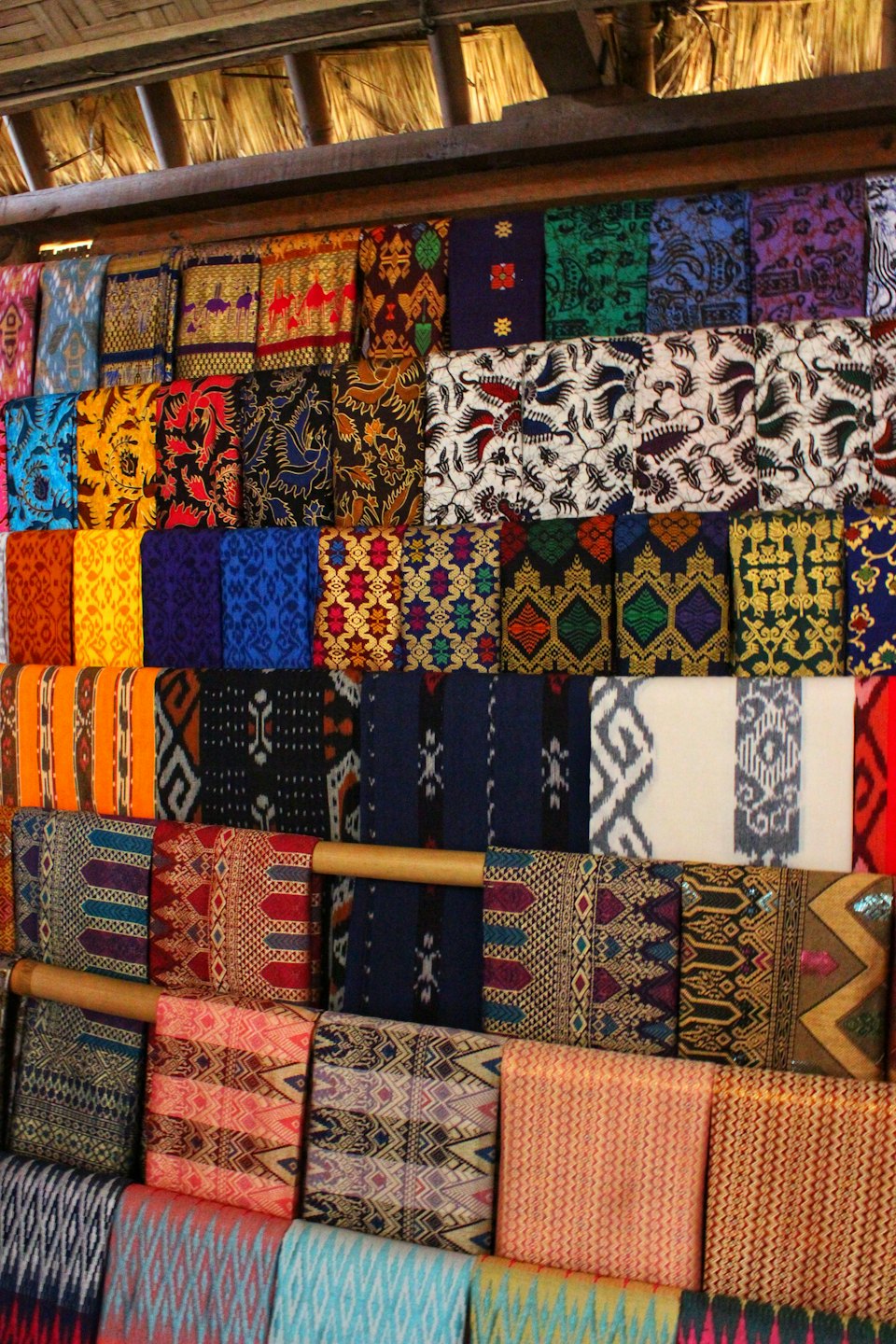 Intricately patterned textiles folded on display in a market stall.