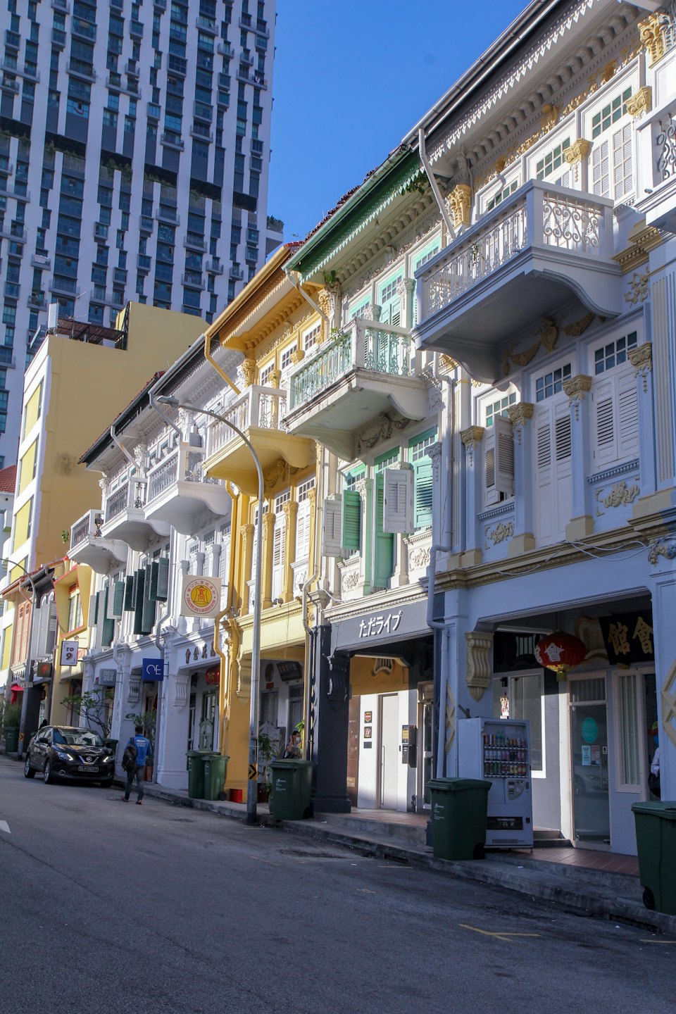 A pedestrian walks past historic shophouses near a modern skyscraper.
