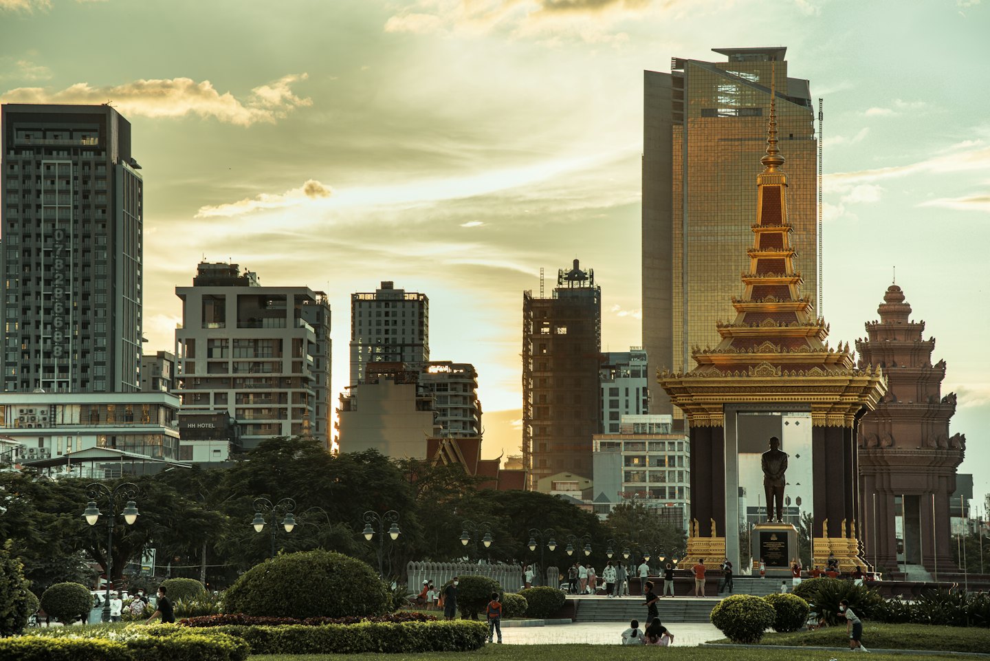 People walk through a park near a golden city monument.