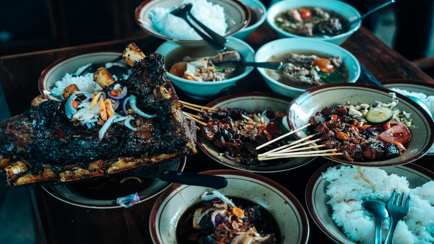 Indonesian grilled ribs and sides arranged on a wooden table.